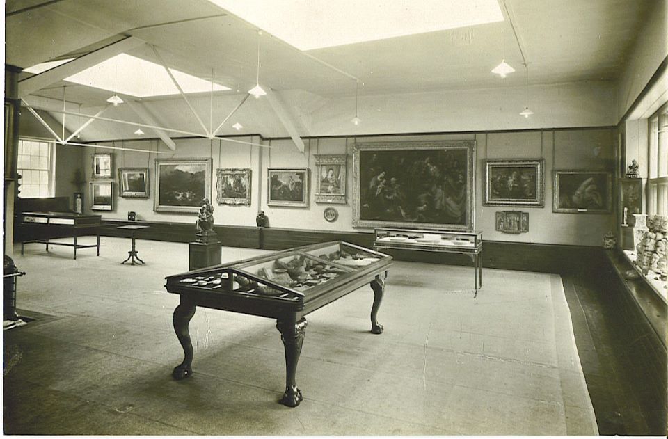 Gallery room with art on the walls and cases in the foreground displaying ceramics.