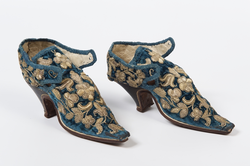 A pair of blue and gold brocade decorated shoes with heels.