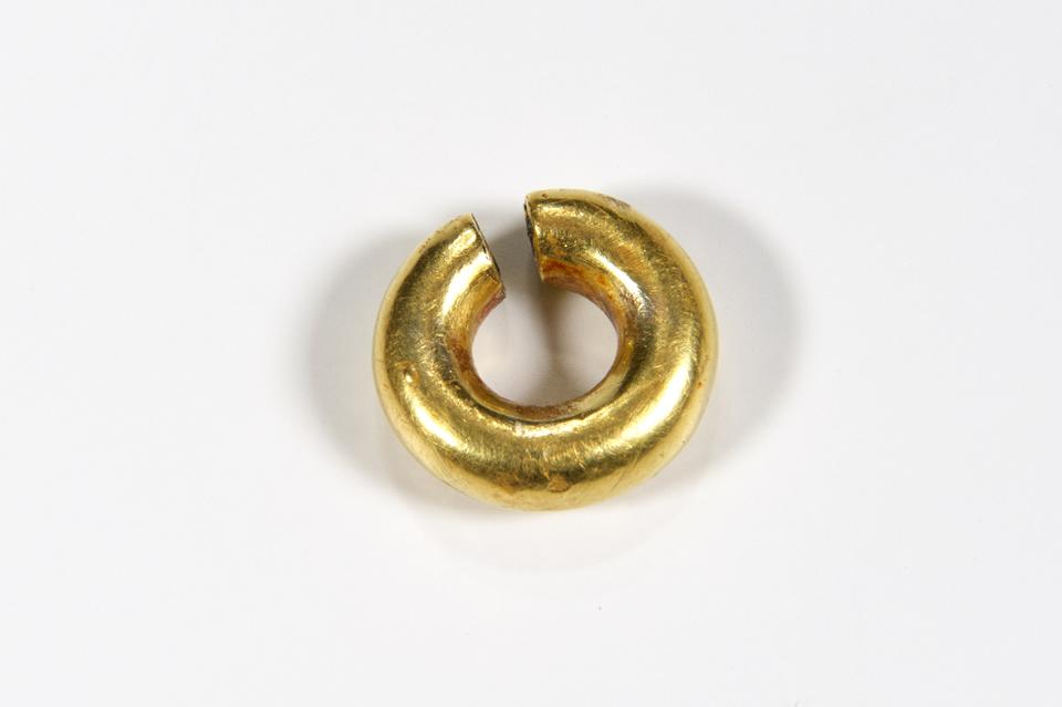 Circular gold shaped with a small gap at the top and hole in the centre.