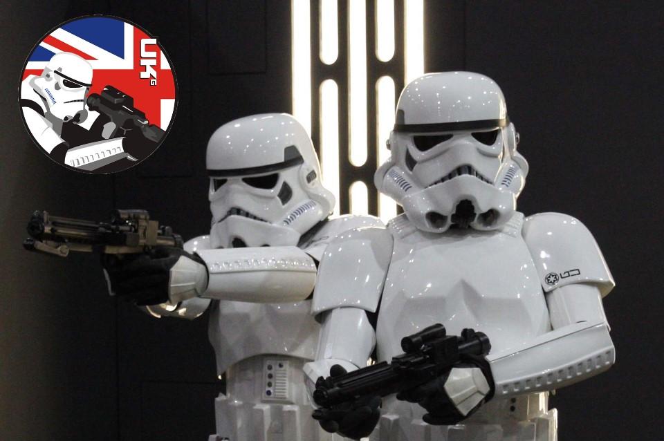 Heads and torso of two stormtroopers from the starwars 501st ukg. They are dressed in white uniforms wearing helmets against a black background. There is a a red and white and blue logo in the top left.