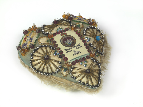 Heart-shaped fabric object studded with decorative pins.