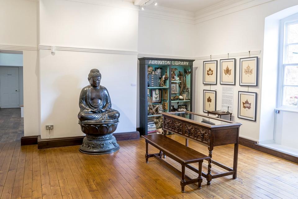 Looking into a room with display case to the far wall and centre  of room. Large Buddha sculpture against far wall.