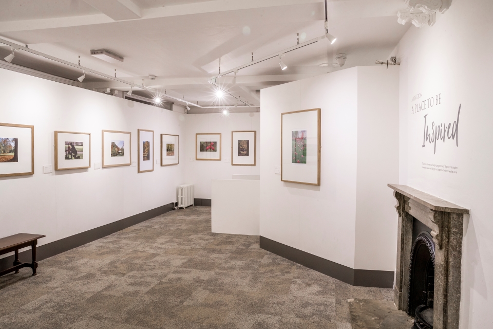 Looking into a room with white walls and artworks hung on the wall. Fireplace in  the right side of this image.