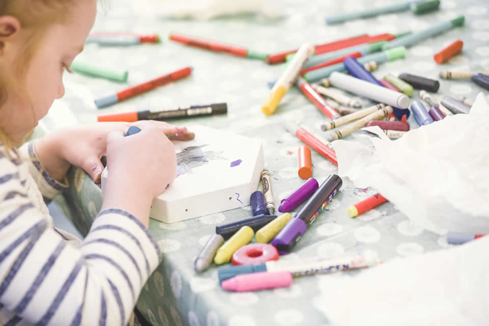 right arm and side on face of child to left of image. Table with crayons in the foreground