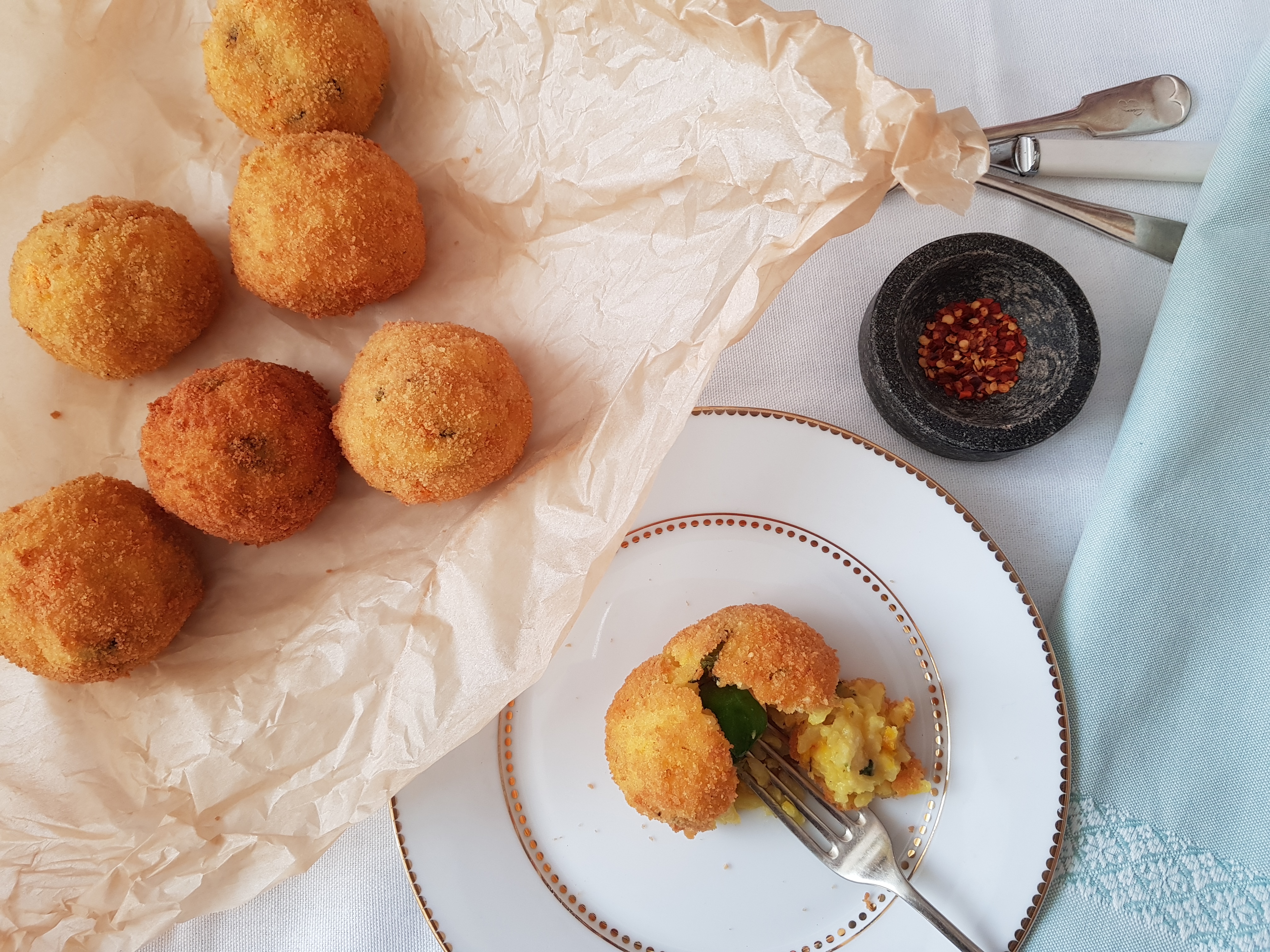 Plate with one ball of arancini on sliced by a fork, Six arnancini on a piece of parchment paper to the side.