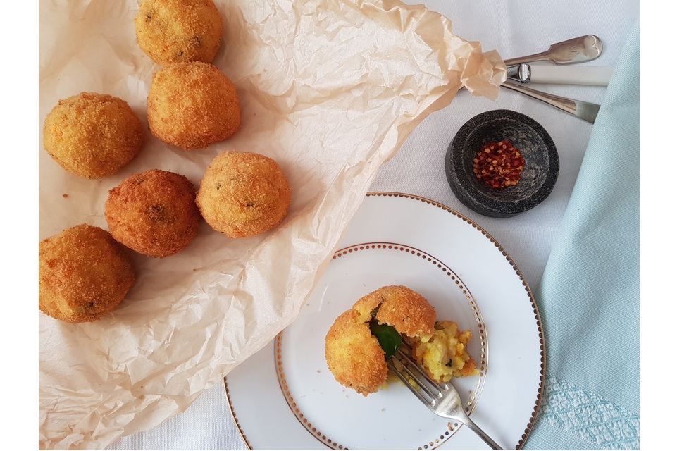 several balls of arancini on parchment paper with one arancini on a plate broken in half by a fork.