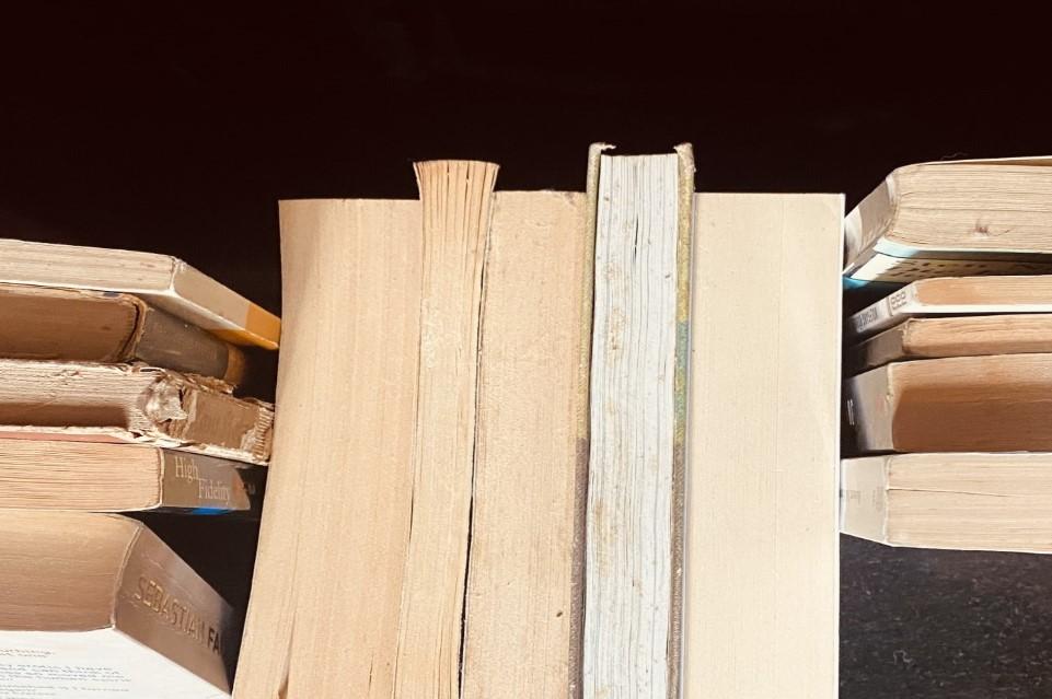 Old books stacked horizontally and vertically with their fore-edges showing, against a black shiny background