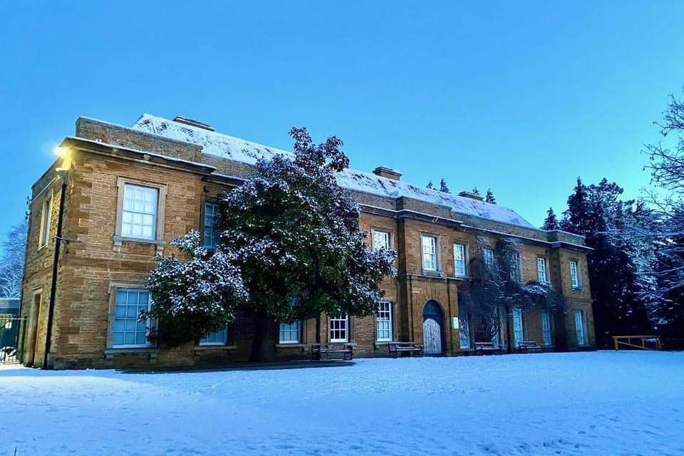 Historic building of honey coloured stone with snow in the foreground and a cold blue sky behind.