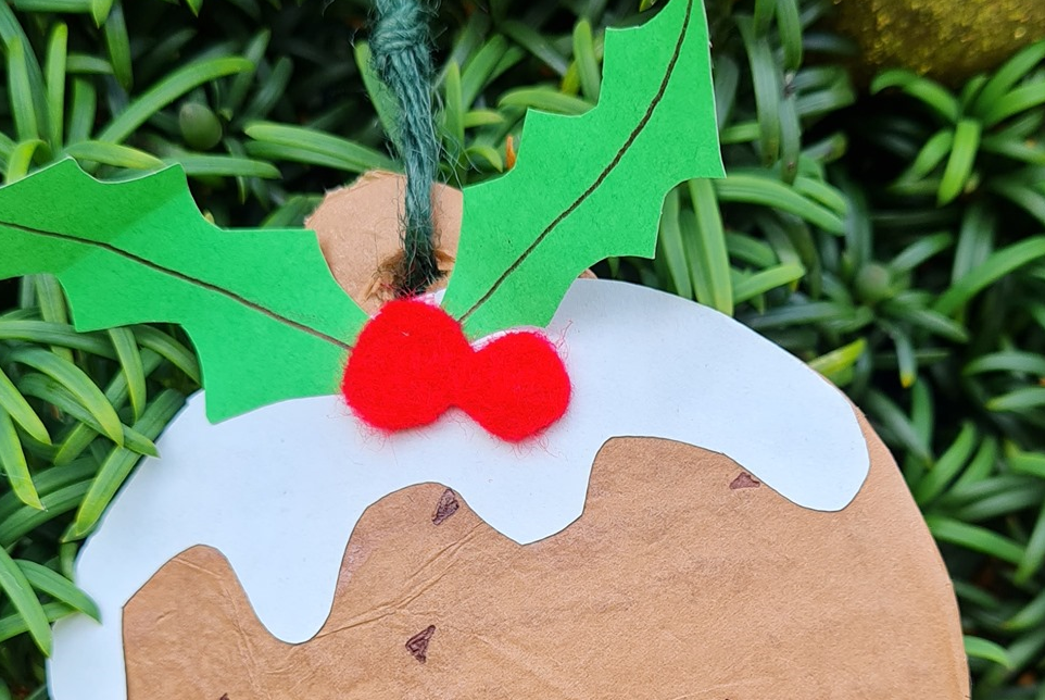 Top of a card crafted chrismas pudding with holly leaves, berries and dripping cream