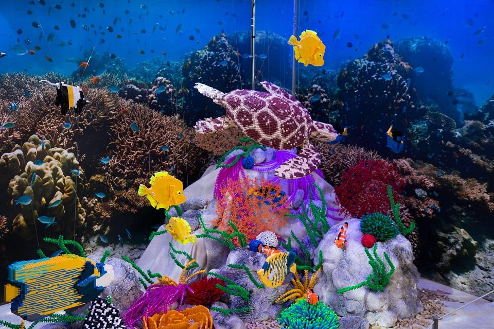 Underwater scene built of lego bricks. Blue background with colourful yellow, purple, green, blue striped fish at the centre front.