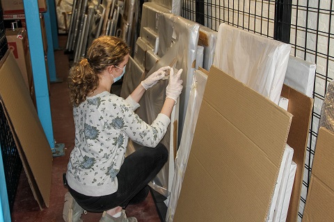 head of woman wearing face mask and gloves looking at a painting.