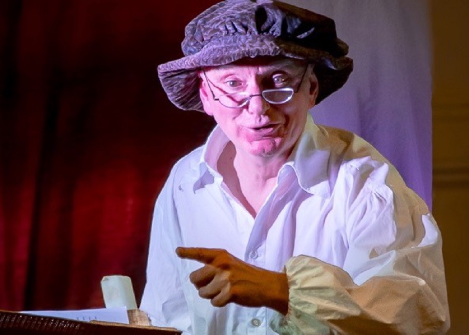 Man in floppy hat and white shirt pointing his finger off to the right.