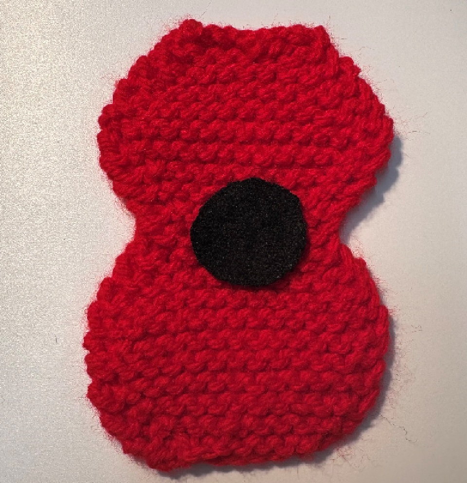 Two petal knitted poppy in red wool with a black felt circle centre