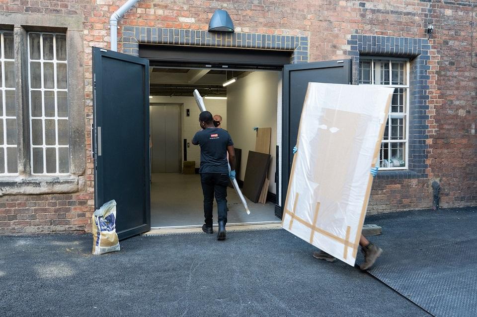 Large white rectangular painting being transported through rectangular opening in a building.