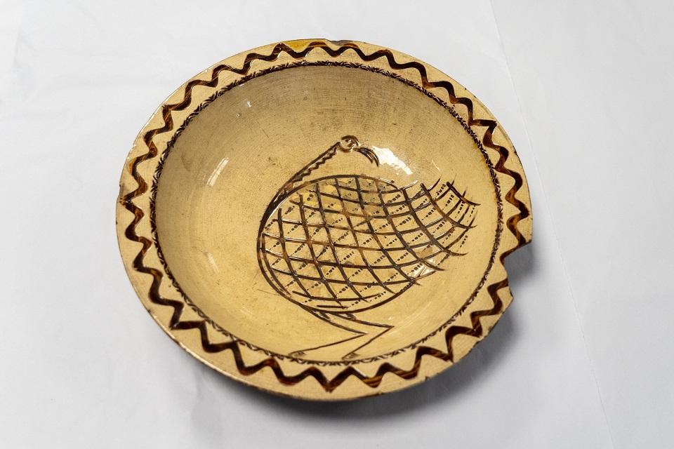 Yellow round plate depicting image of large rounded bird picked out in brown slipware. Repeat pattern to edge.