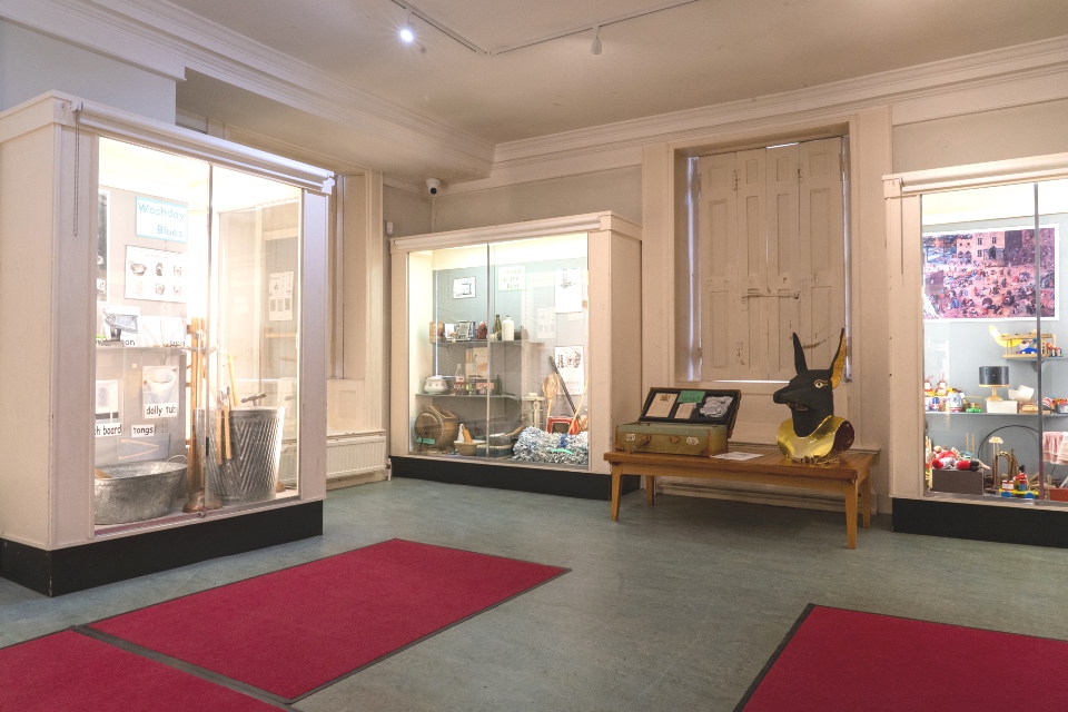 Room with two large glass display cases with museum objects. Two red mats on the foreground floor.