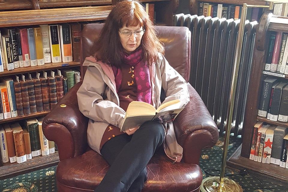 Seated figure sitting in front of library shelves reading a book.