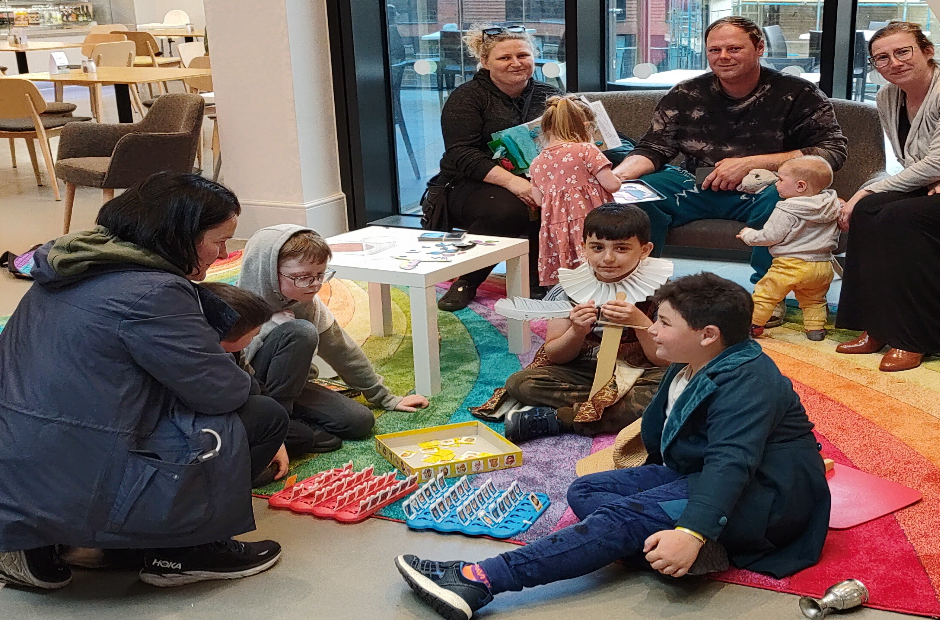 Image showing children and adults stting on a colourful red mat with a glass window behind.