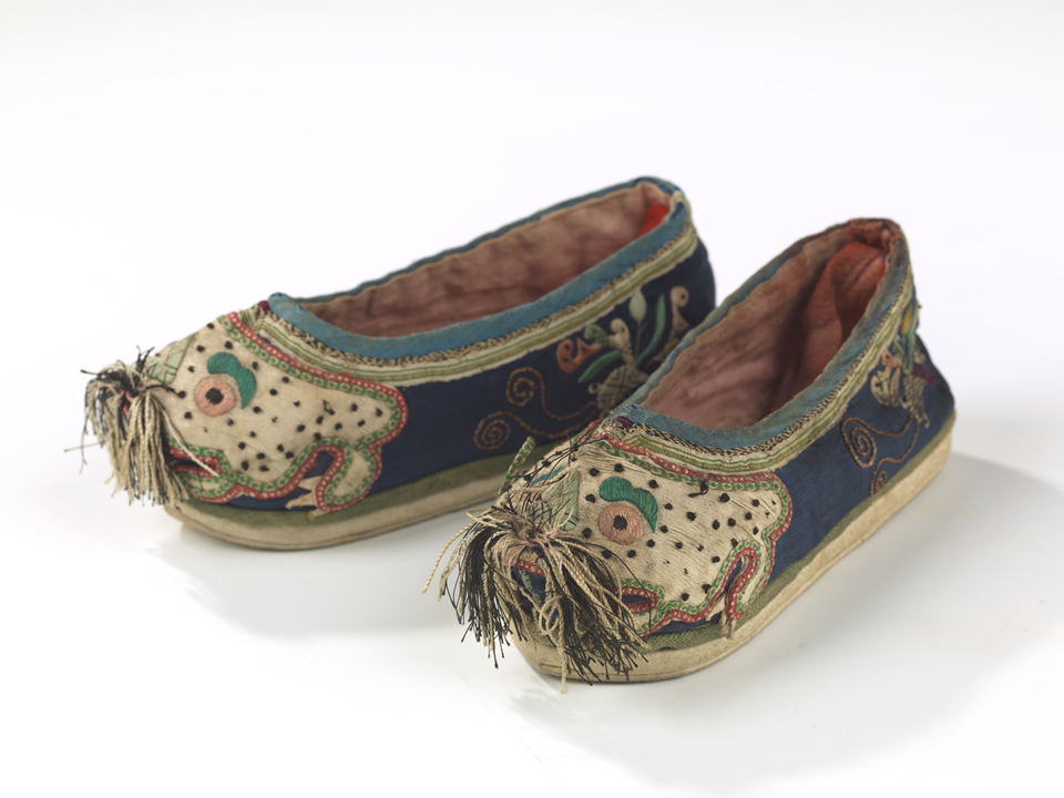 Two shoes angled towards the camera with tiger faces and fabric tassels.