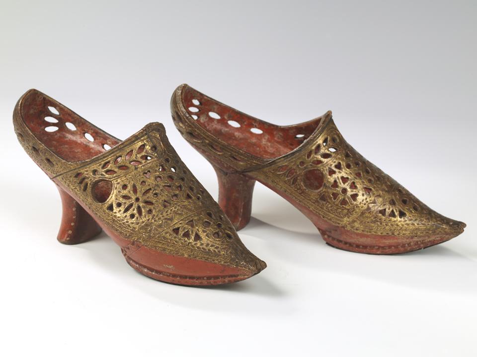 Pair of shoes with heals and cutouts in gold with red internal area.