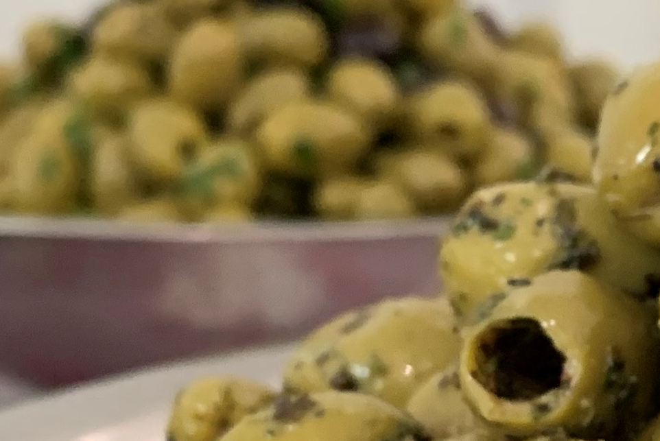 Close up of a bowl of green olives covered with green herbs