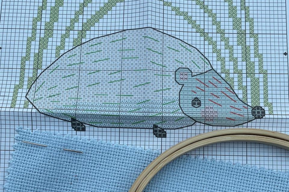 Cartoon cross stitched bear with cross stich pine trees in background