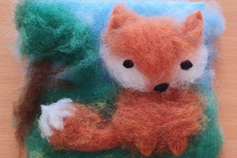 Photo of crafted fox made of colourful fluffy wool. The fox looks out from the image and there is a tree to the left.