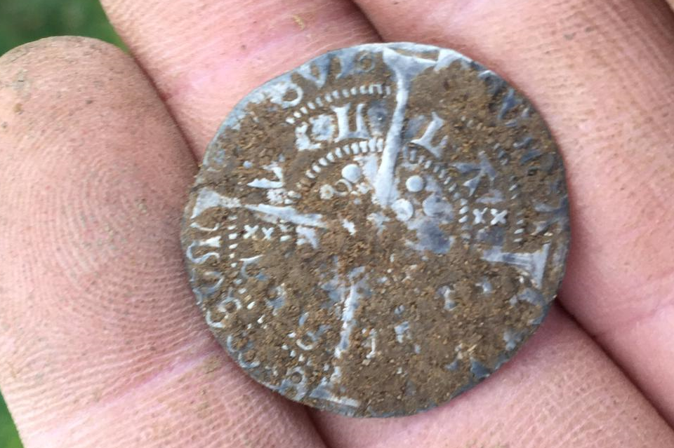 Circular silver coin with cross motif sitting on two fingers.