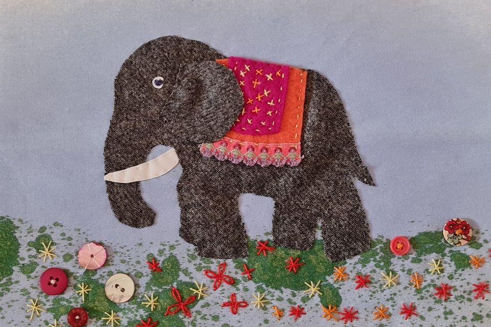 Grey fabric elephant with colourful red saddle.