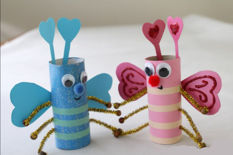 Photo of one blue and one pink stripey cardboard tube bug with googly eyes and pompom noses. Heart shaped antenna, heart shaped wings and glittery bendy arms.