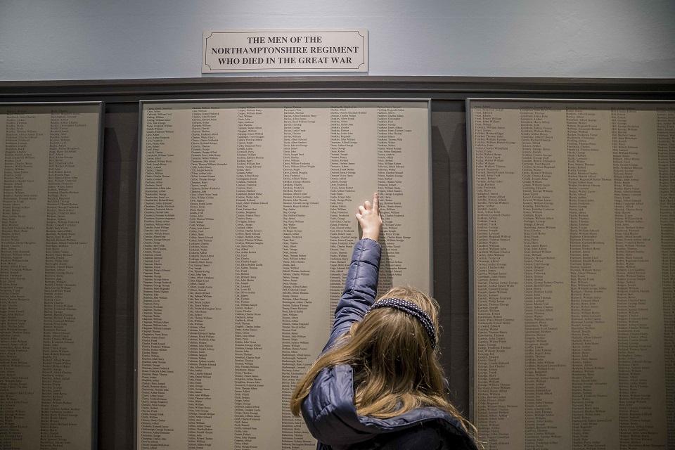 Girl with long hair and back to camera pointing upwards whilst looking at panel with text.