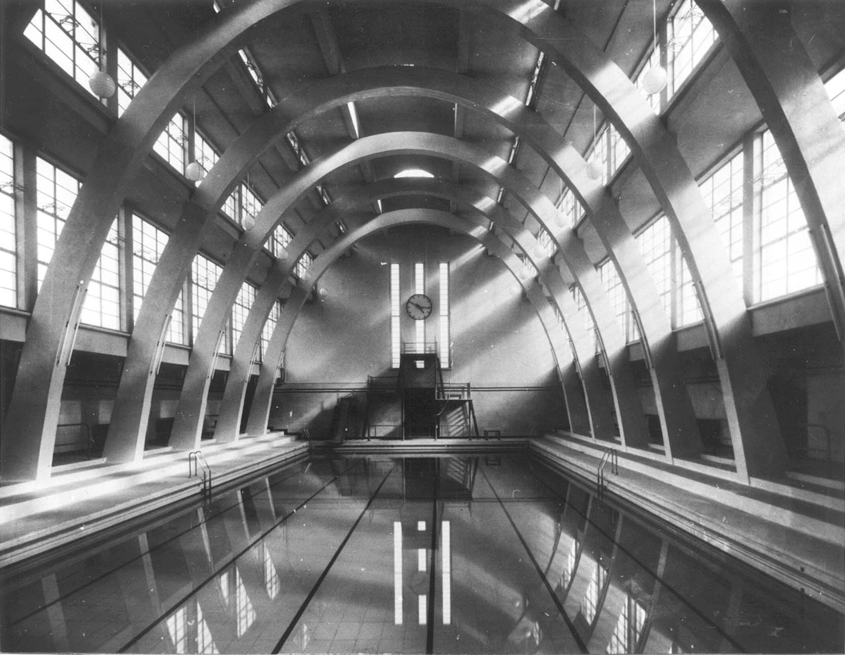 Black and white photograph depicting curved glazed roof with radial solid supports and water of pool at bottem.