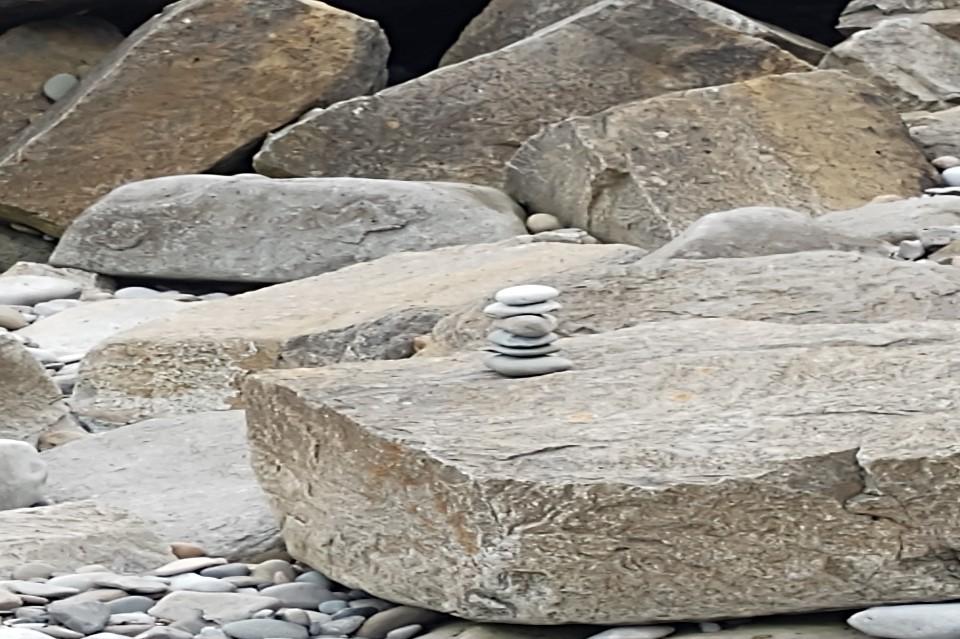 Large flat rock in bottom right in a pebble beach landscape, Pebbles piled in a tower on top of the flat rock.