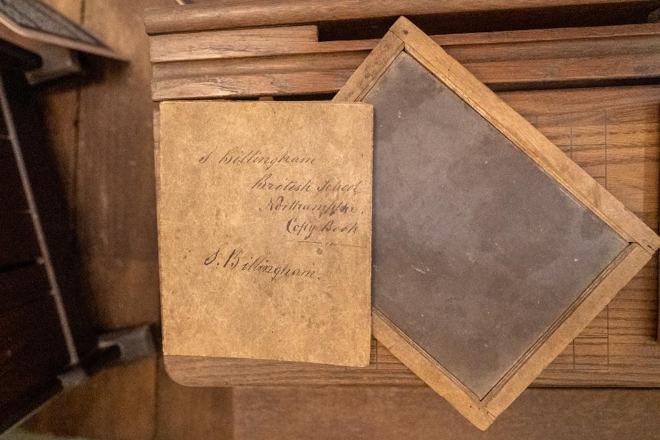 Wooden desktop in the background displaying wood rimmed dark slate at an angle and a brown paper copy book.