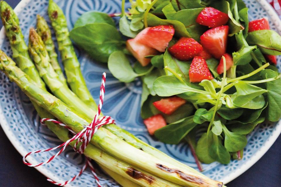 Photograph depicting green and white asparagus curved on the left of a blue plate. Red radishes with green leaves on the right of the image.