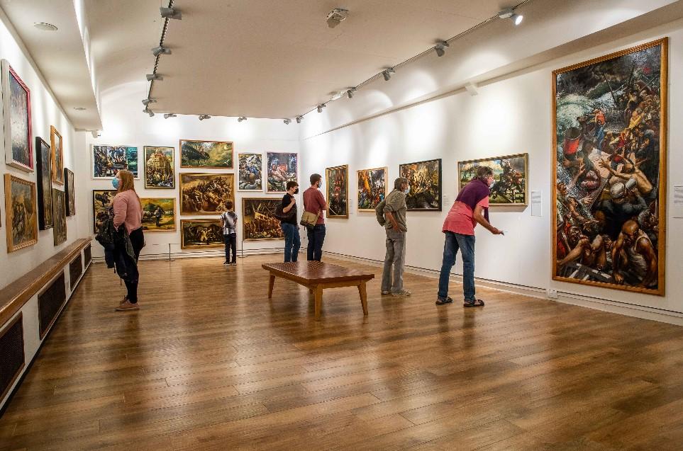 Group of people looking at colourful paintings on the walls of a gallery