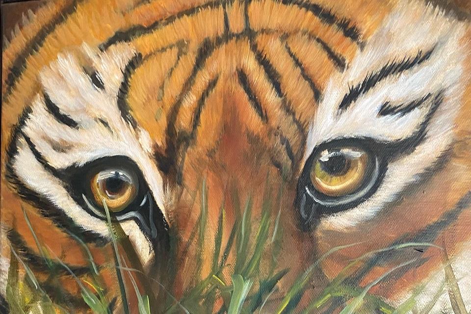 Painted image of the face of a tiger looking directly at the viewer. Green grass in the foreground.