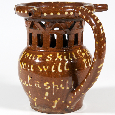 A brown puzzle jug decorated with writing and cut out holes