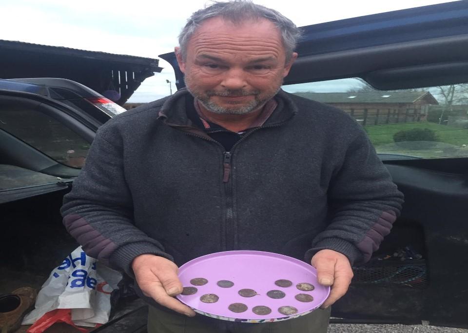 Man standing in fromt of car holding purple circular tray of round coins.