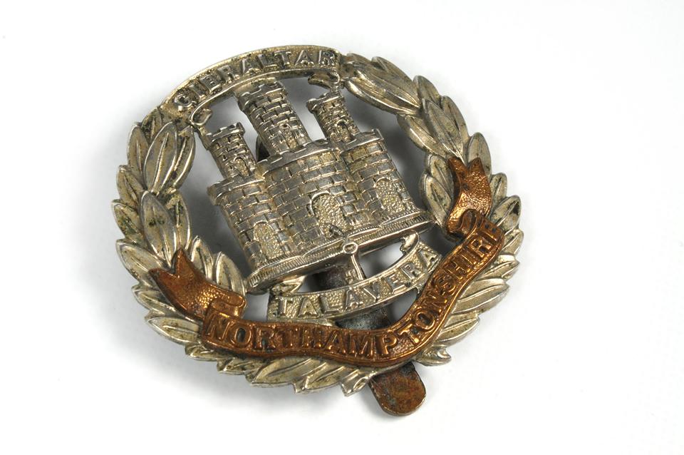 small round badge depicting a castle surrounded by leaves forming a wreath shape