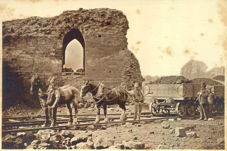 Photograph of the Postern Gate at Northampton Castle Glued to one page of an album which had a linen hinge. Shows a small section of wall and postern gate, with three small boys sitting on the top. 