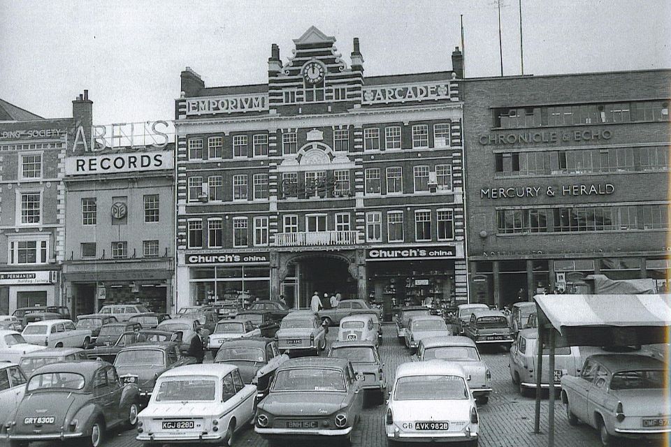 Large 5 storey building with decorative clock in the background. Rows of cards parked in the foreground.