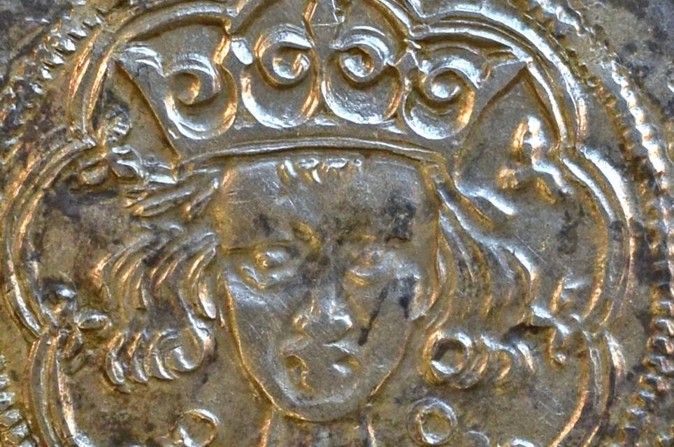 Silver imbossed image of a head with a crown from a coin.