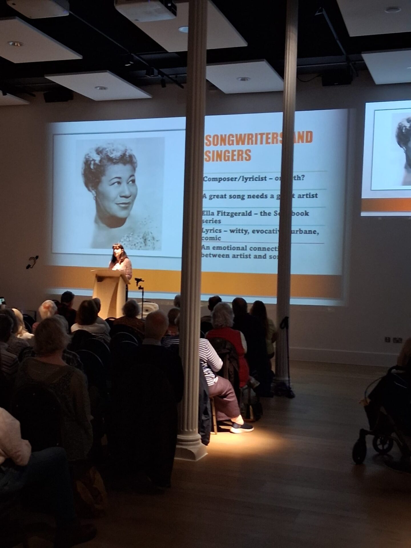 speaker in front of an audience with image of woman behind and writing
