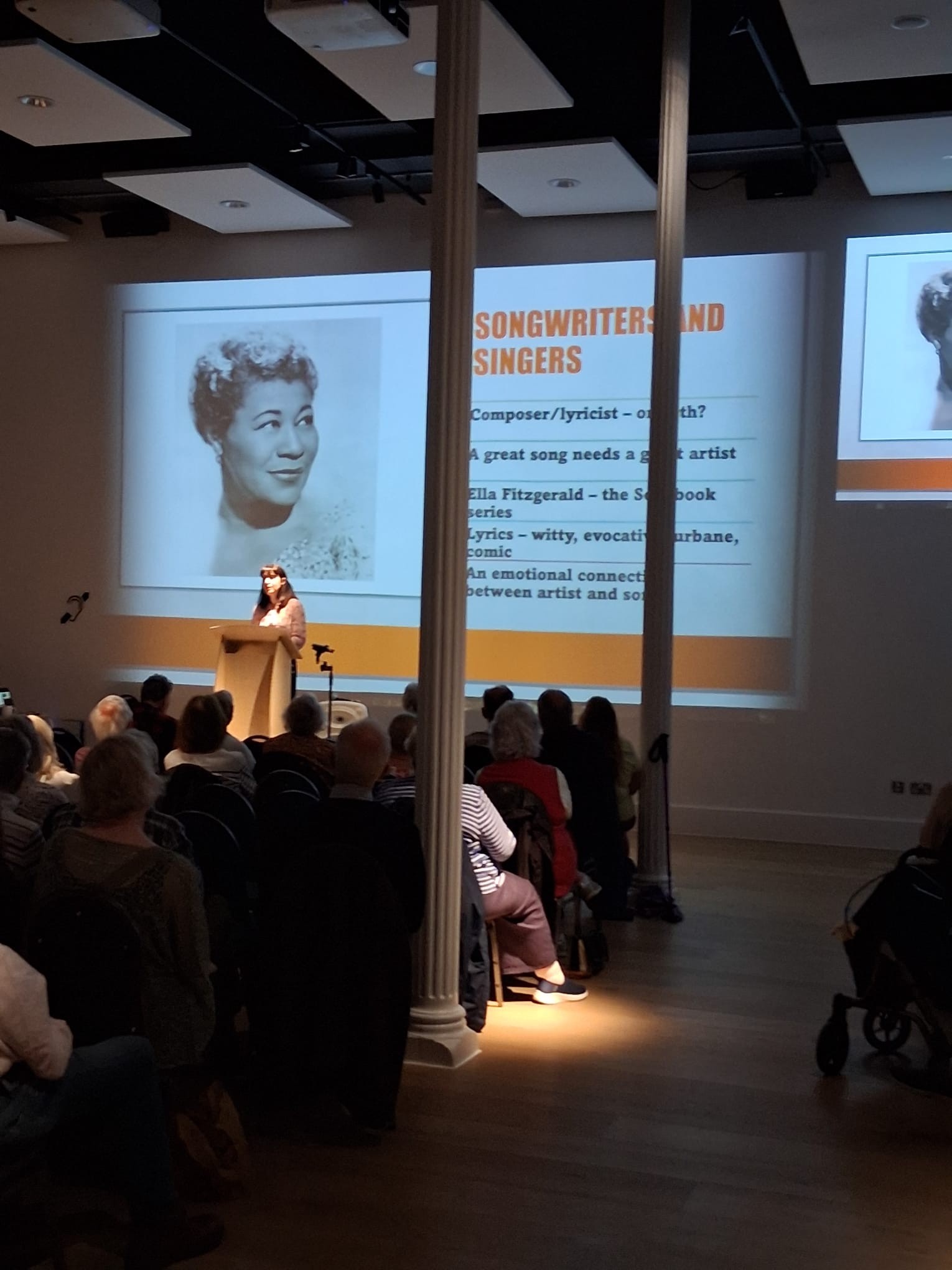 talk image 5 speaker in front of an audience with image of woman behind and writing