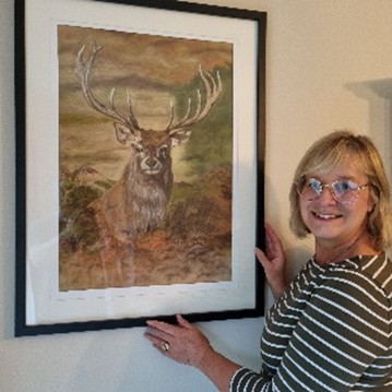 Person standing beside a framed painting of a stag with large antlers mounted on a wall.