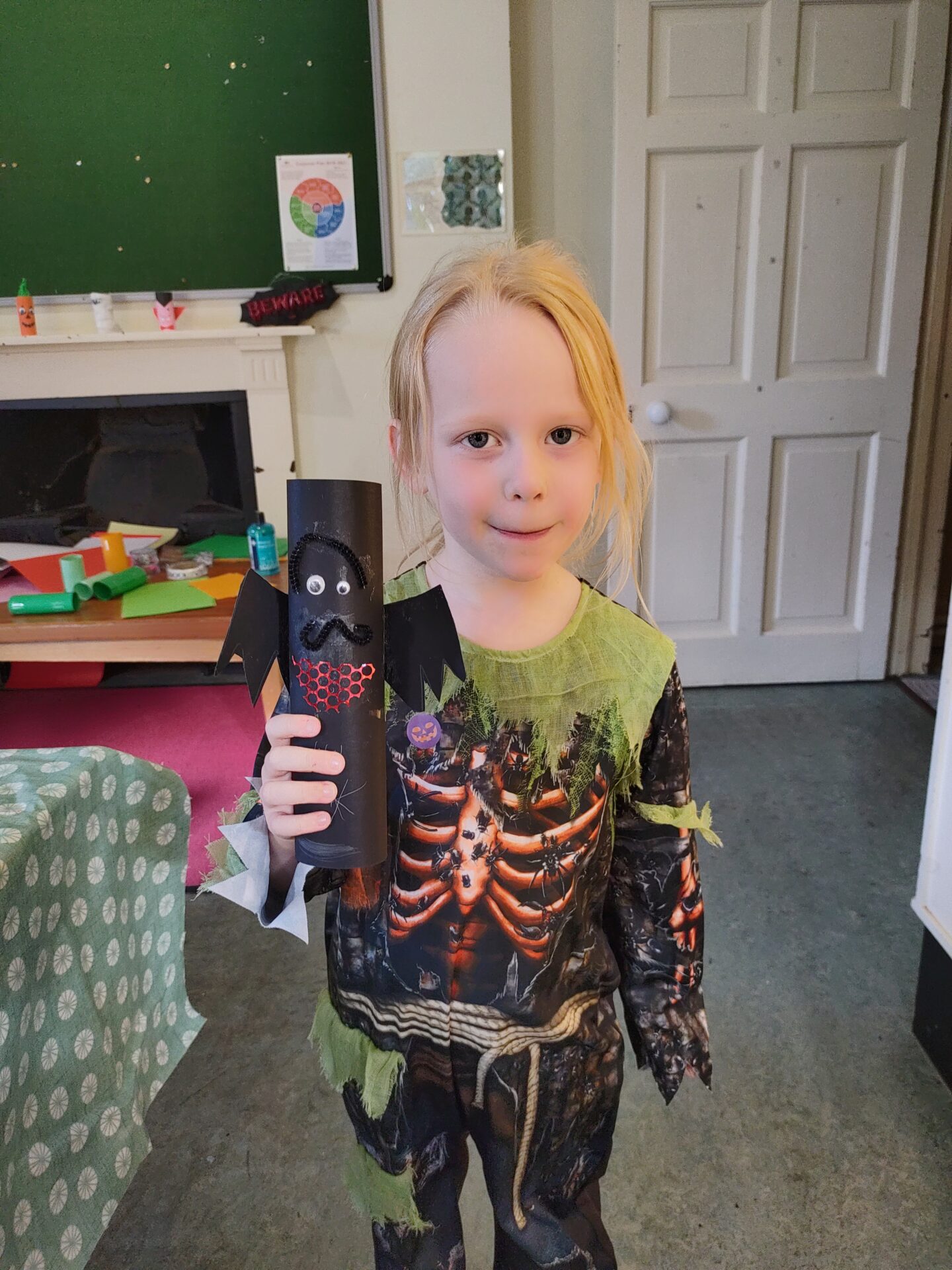 IMG_20211030_130522 Child holding a handmade bat craft while wearing a Halloween costume.